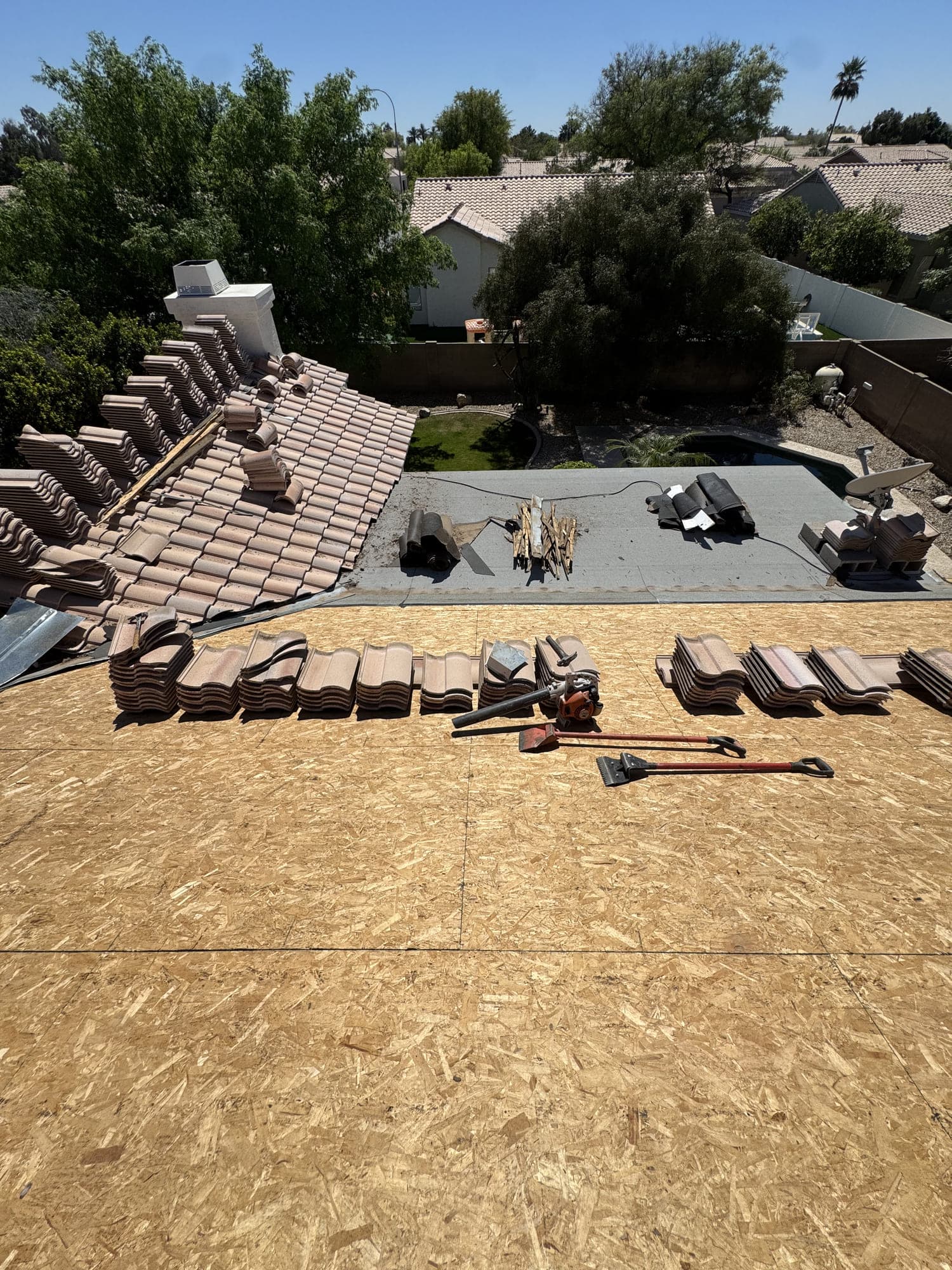 A pitched tile slope meeting a low-slope section on the same house — the flat area coated, the tile side stripped to new decking, with lifted tile and tear-off tools laid across it.