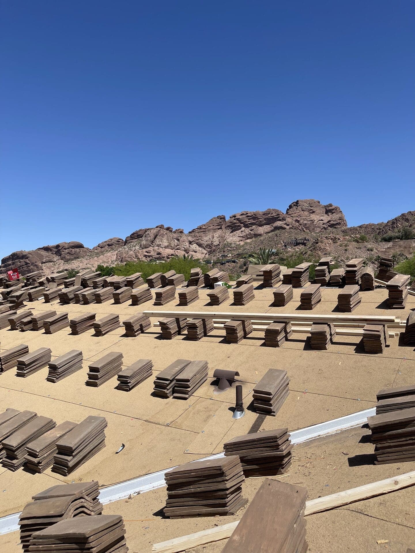 Roof tiles staged in rows on underlayment during a tile roof installation, red rock mountain behind